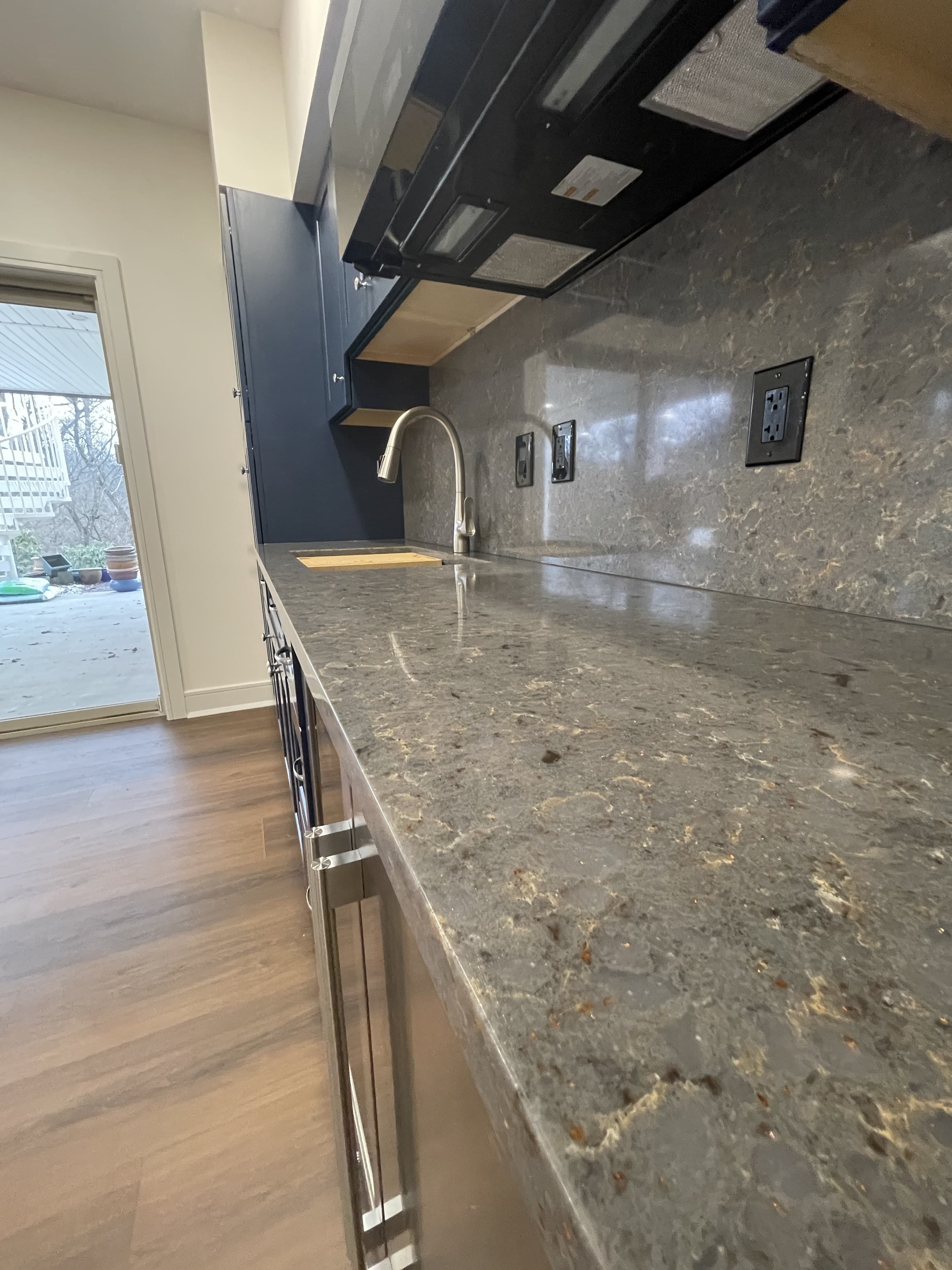 Gray patterned countertop and matching backsplash beside blue cabinets and a sink faucet.