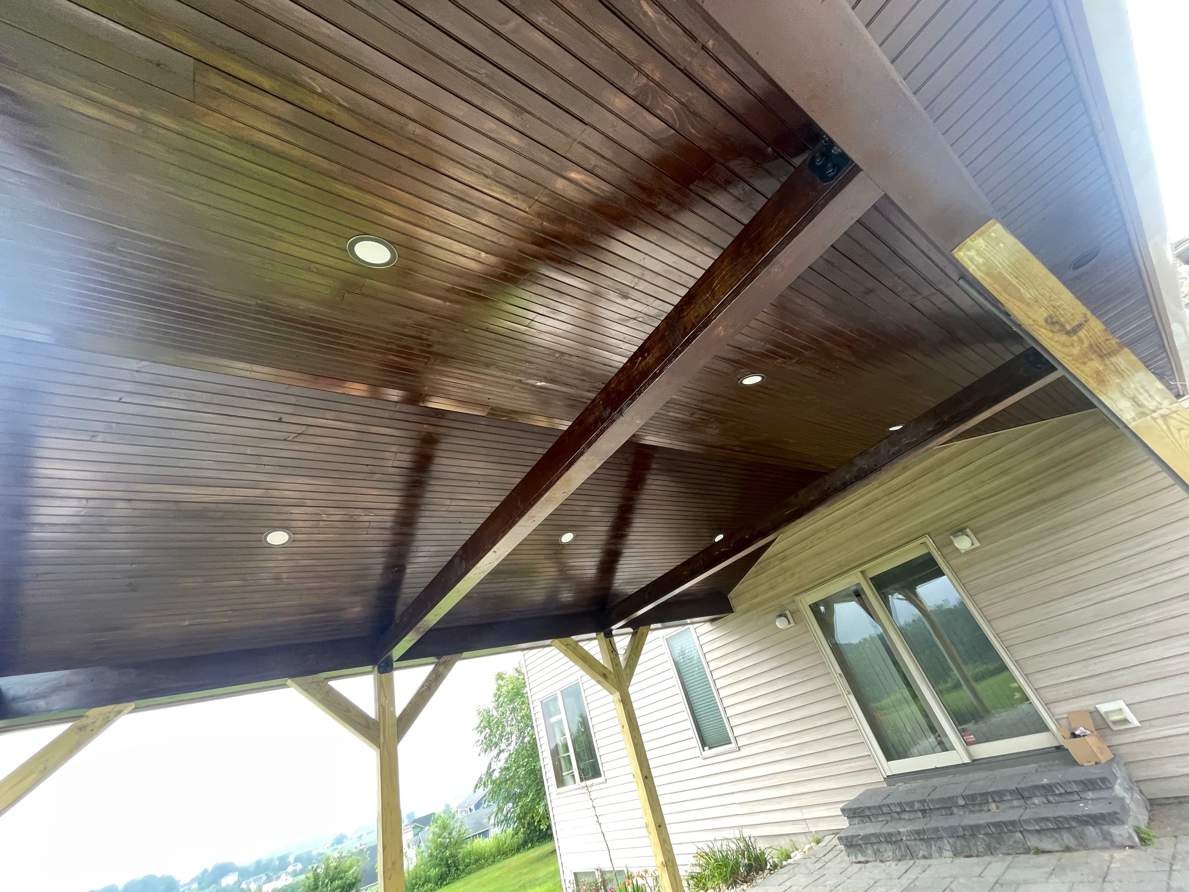 Wood pavilion ceiling with dark beams and recessed lights, viewed from below.
