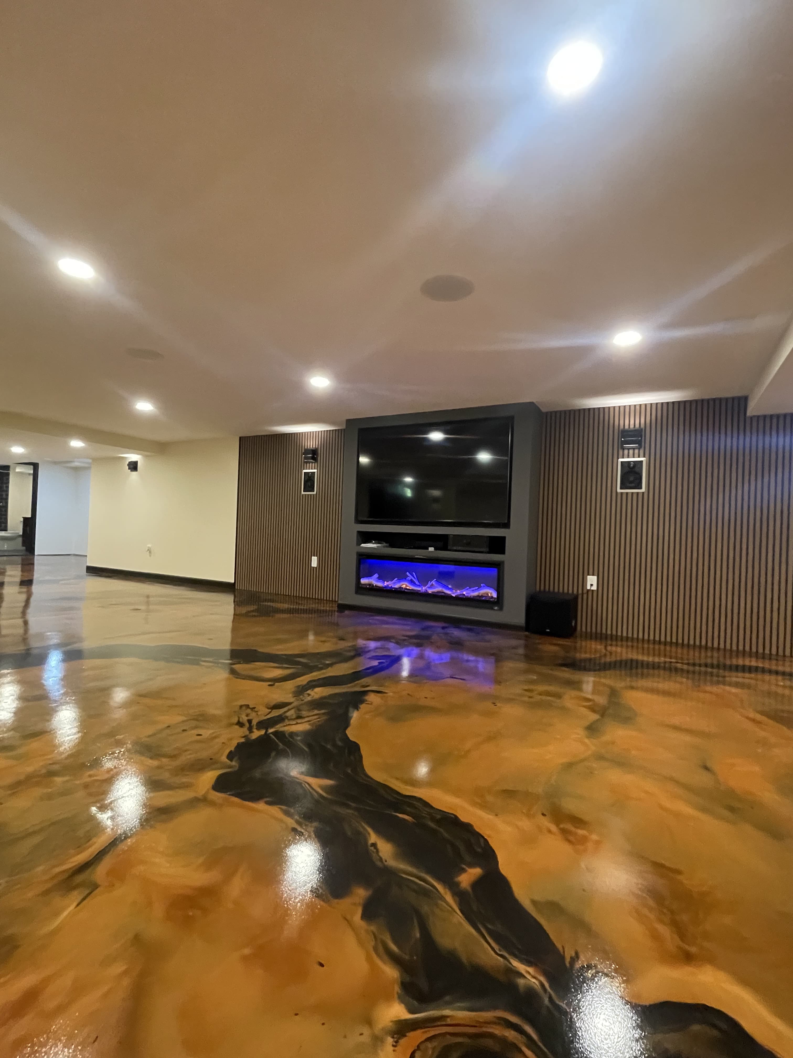 Glossy floor with gold and dark flowing patterns in front of a basement media wall.